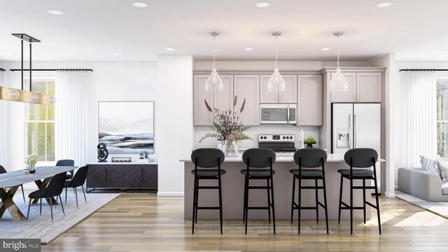 kitchen with gray cabinets, appliances with stainless steel finishes, an island with sink, a kitchen bar, and decorative light fixtures