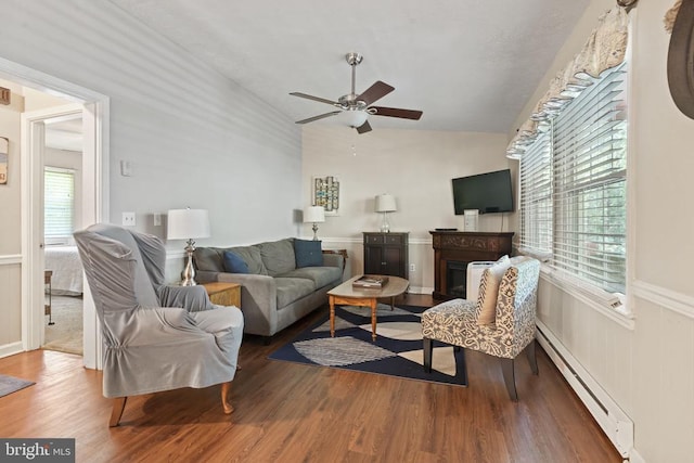 living room with a wainscoted wall, a baseboard heating unit, a glass covered fireplace, wood finished floors, and lofted ceiling