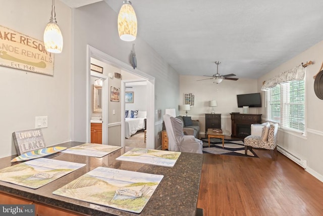 dining space featuring ceiling fan, a fireplace, a baseboard heating unit, and dark wood-type flooring