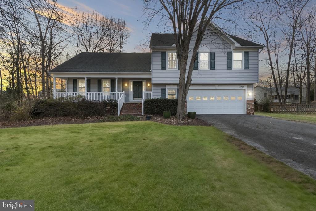 tri-level home featuring a garage, a lawn, and covered porch