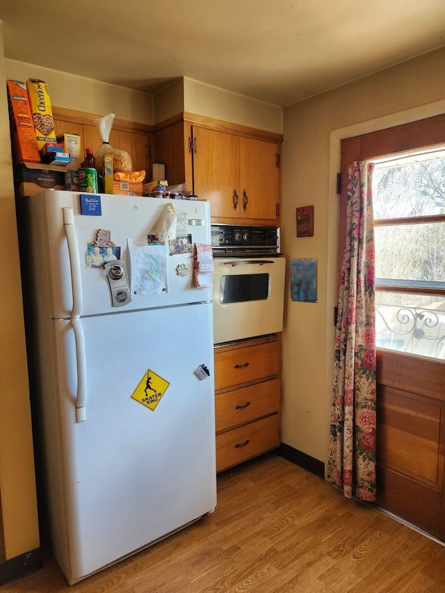 kitchen with white appliances, brown cabinets, and light wood-style flooring