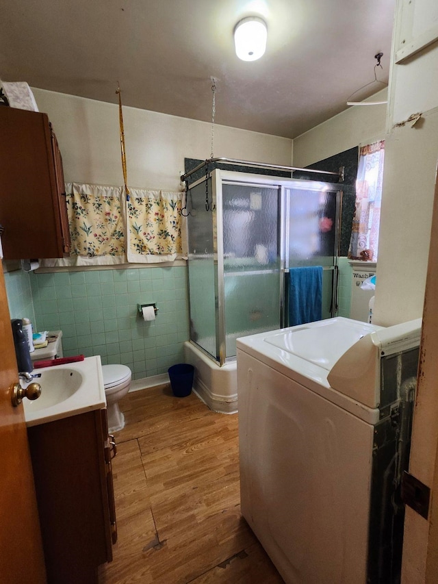 bathroom with washer / dryer, wood finished floors, vanity, a shower stall, and tile walls