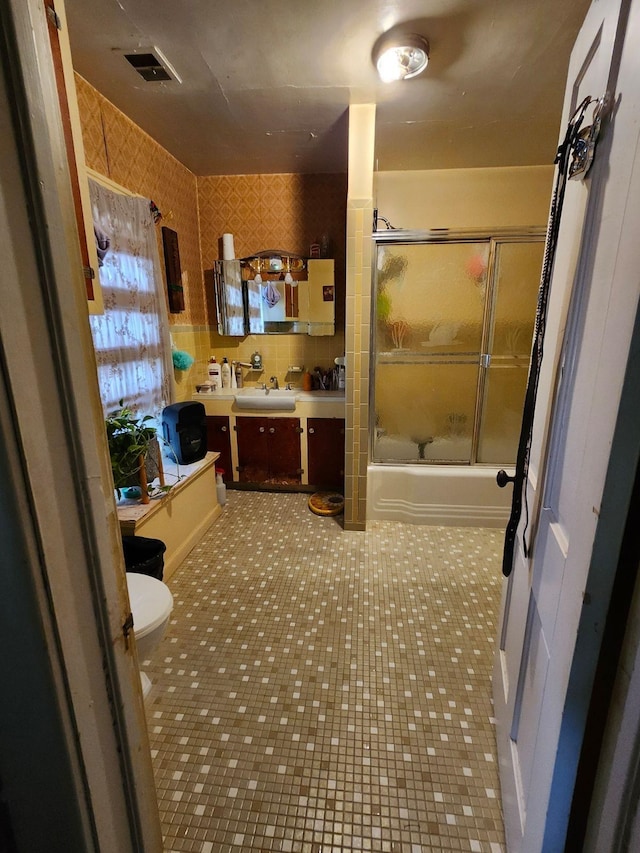 bathroom featuring shower / bath combination with glass door, visible vents, toilet, vanity, and tile patterned floors