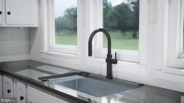 details featuring tasteful backsplash, dark countertops, white cabinets, and a sink