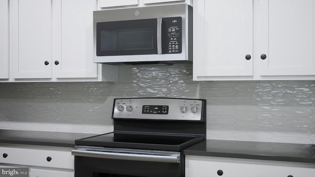 kitchen featuring appliances with stainless steel finishes, dark countertops, white cabinets, and tasteful backsplash