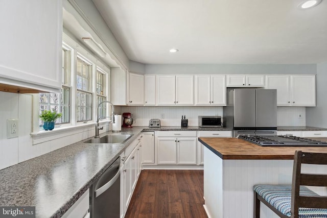 kitchen with a sink, butcher block countertops, stainless steel appliances, white cabinetry, and dark wood-style floors