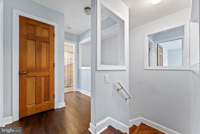 hall with baseboards, an upstairs landing, and dark wood-style flooring