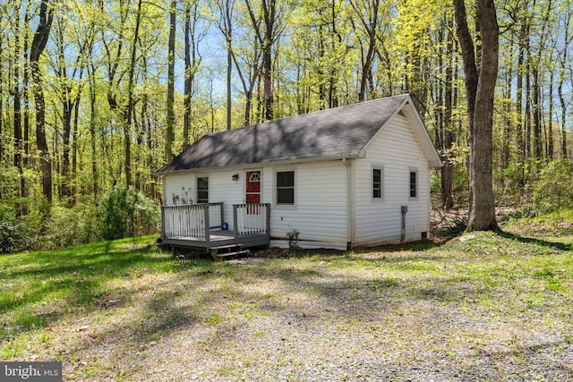 view of front of home featuring a wooden deck, a forest view, and roof with shingles