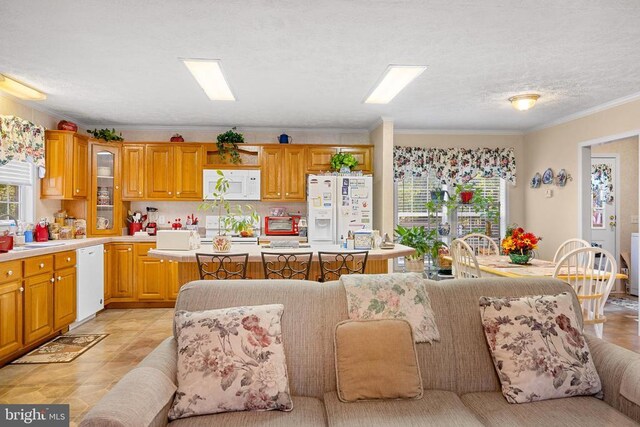 kitchen featuring white appliances, a breakfast bar area, a center island, ornamental molding, and light tile patterned flooring