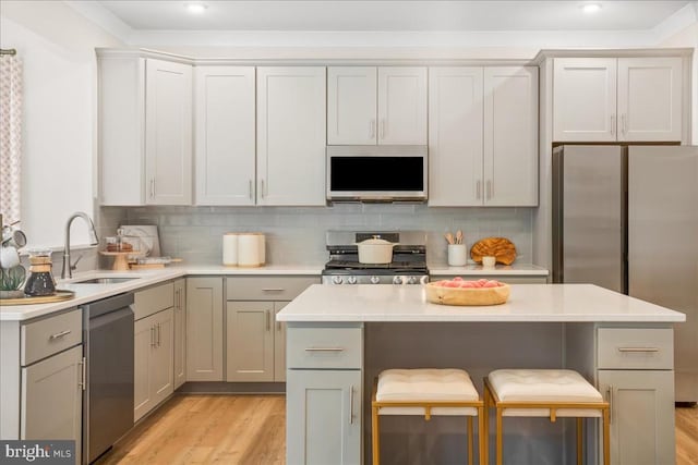 kitchen with appliances with stainless steel finishes, sink, a kitchen breakfast bar, decorative backsplash, and light wood-type flooring