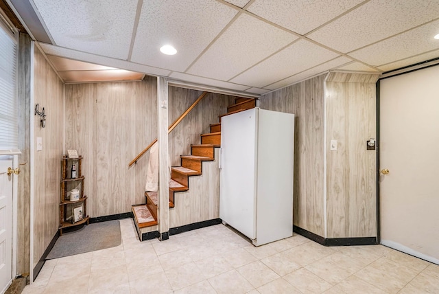 basement featuring wooden walls, a paneled ceiling, and white refrigerator