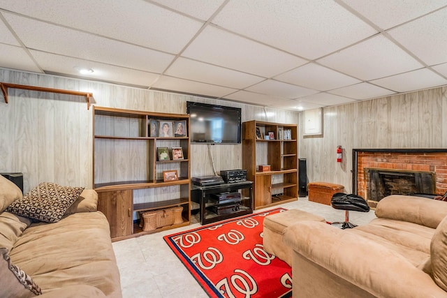 living room featuring a paneled ceiling, a brick fireplace, and wood walls