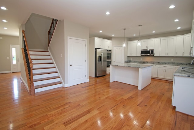 kitchen with pendant lighting, white cabinetry, stainless steel appliances, a center island, and light stone counters