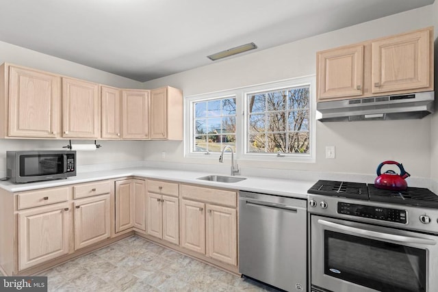 kitchen with under cabinet range hood, a sink, light countertops, appliances with stainless steel finishes, and light brown cabinetry