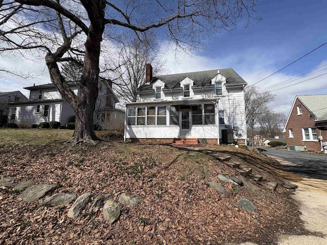 view of front of home with a sunroom, a chimney, and central air condition unit