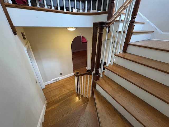 staircase featuring arched walkways, wood finished floors, visible vents, and baseboards