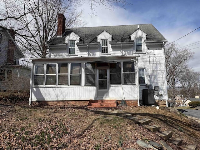 view of front facade with entry steps, a sunroom, a chimney, and central AC unit