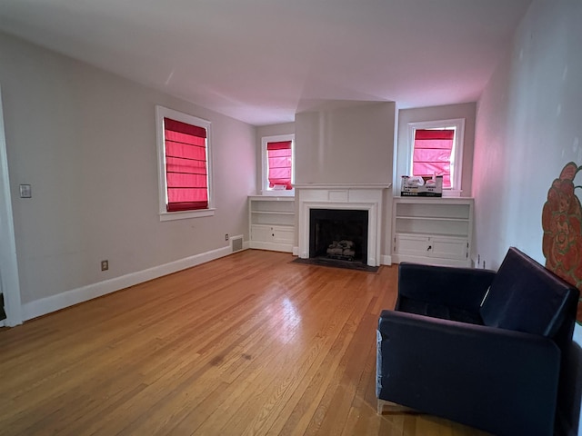 living area with light wood-style flooring, a fireplace with flush hearth, visible vents, and baseboards