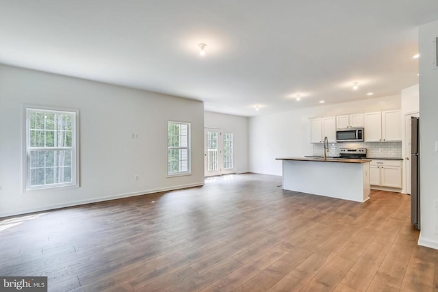 kitchen featuring appliances with stainless steel finishes, a kitchen island with sink, light hardwood / wood-style floors, white cabinets, and decorative backsplash