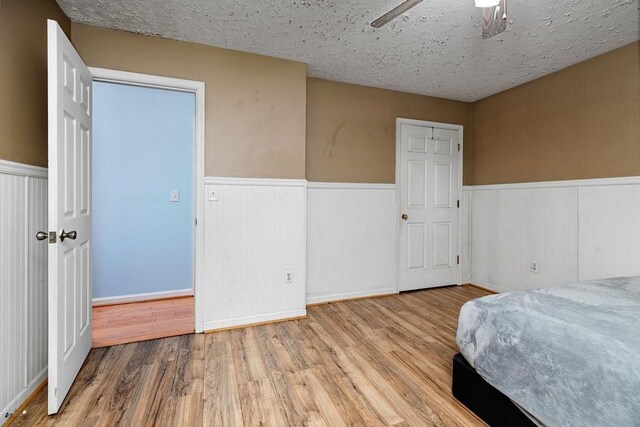 bedroom featuring wood finished floors, a textured ceiling, and a wainscoted wall