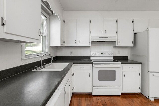 kitchen with a sink, dark countertops, under cabinet range hood, and white appliances