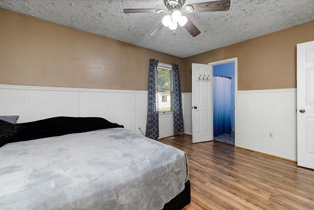 bedroom with a textured ceiling, ceiling fan, wainscoting, and wood finished floors