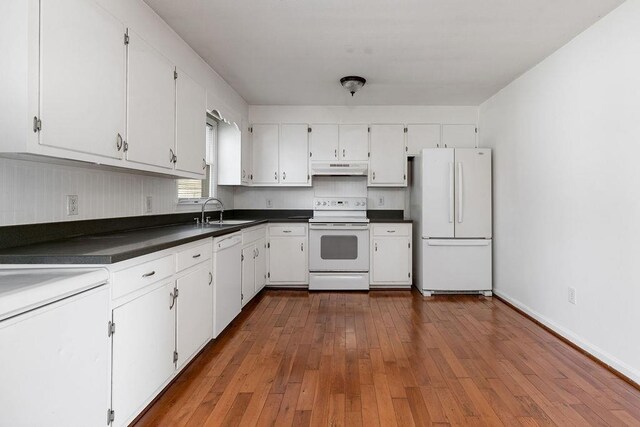 kitchen featuring dark countertops, a sink, under cabinet range hood, white appliances, and white cabinetry