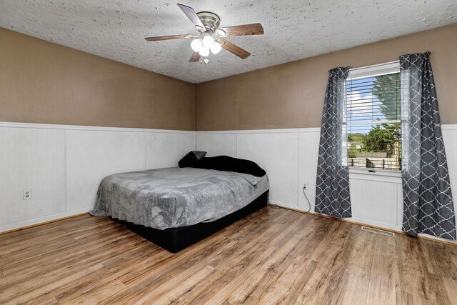 bedroom featuring a textured ceiling, wainscoting, wood finished floors, and visible vents