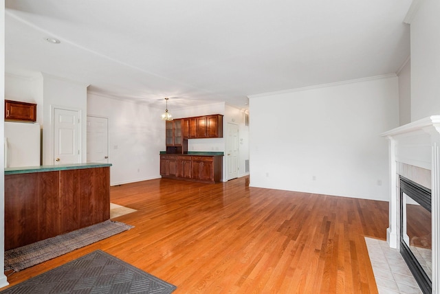 unfurnished living room with ornamental molding, a notable chandelier, a fireplace, and light hardwood / wood-style floors