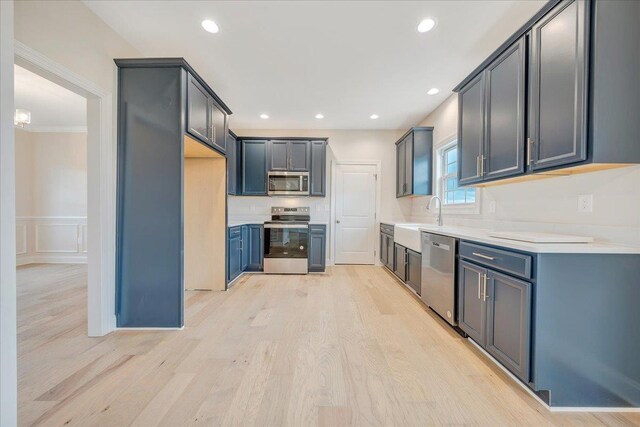 kitchen with appliances with stainless steel finishes, sink, and light hardwood / wood-style flooring