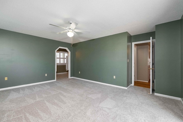 carpeted empty room featuring baseboards, a ceiling fan, and arched walkways