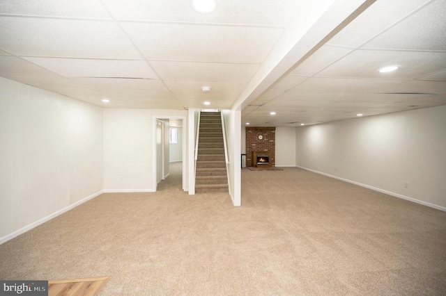 finished basement featuring a drop ceiling, baseboards, light colored carpet, and stairs