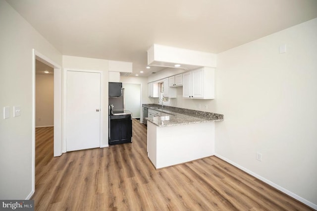 kitchen with wood finished floors, baseboards, a peninsula, a sink, and white cabinetry