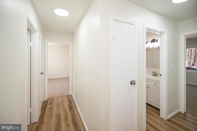 hallway with a sink, baseboards, and light wood-style flooring