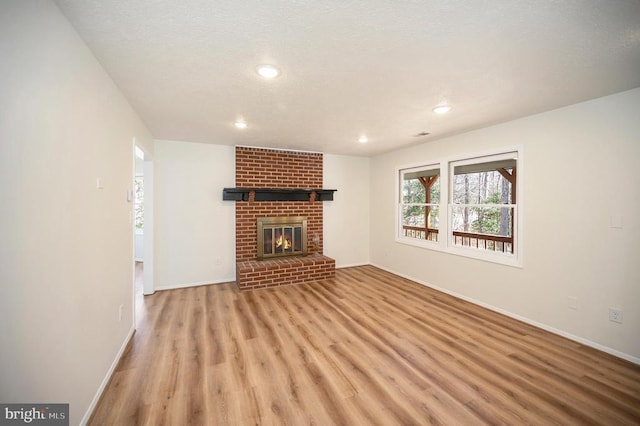 unfurnished living room with a brick fireplace, a textured ceiling, baseboards, and wood finished floors