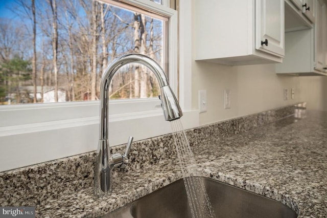 details with white cabinetry, dark stone counters, and a sink