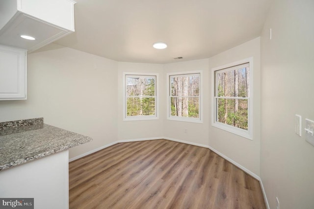 unfurnished dining area featuring plenty of natural light, visible vents, light wood-style flooring, and baseboards