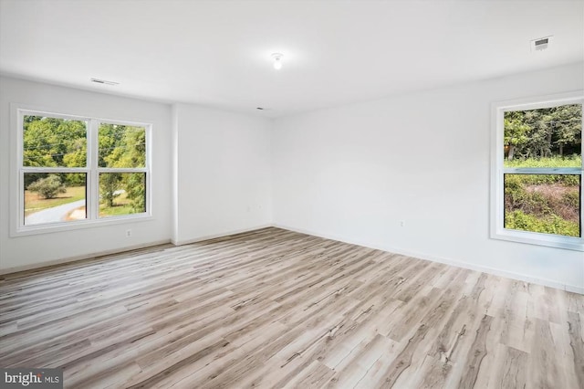 unfurnished room with visible vents, a healthy amount of sunlight, light wood-type flooring, and baseboards