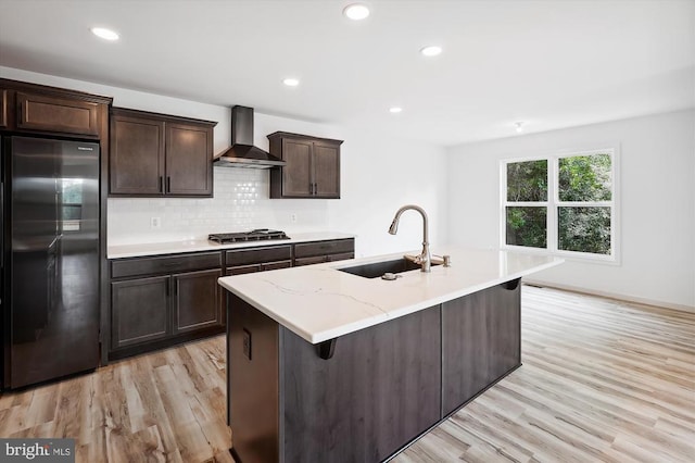 kitchen featuring a sink, stainless steel appliances, light wood finished floors, and wall chimney range hood