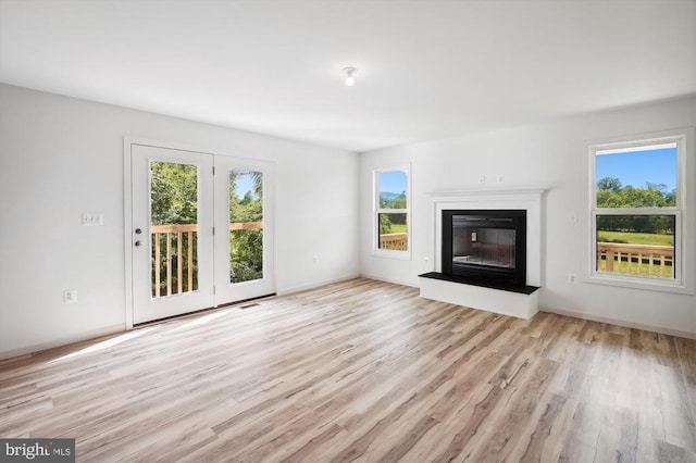 unfurnished living room featuring a glass covered fireplace, light wood-type flooring, and baseboards