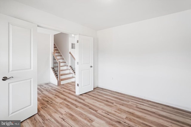 spare room with stairs, light wood-style floors, and visible vents