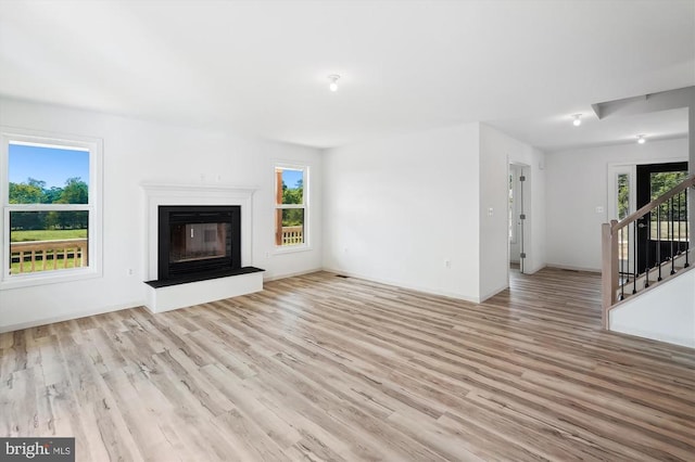 unfurnished living room featuring a glass covered fireplace, a wealth of natural light, wood finished floors, and stairs