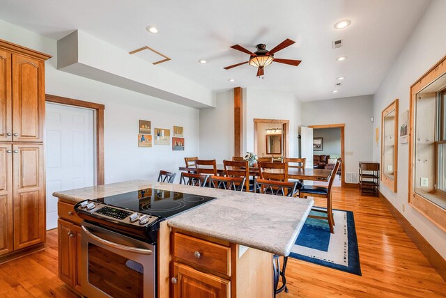 kitchen featuring stainless steel electric range oven, a kitchen island, a breakfast bar, ceiling fan, and light hardwood / wood-style floors