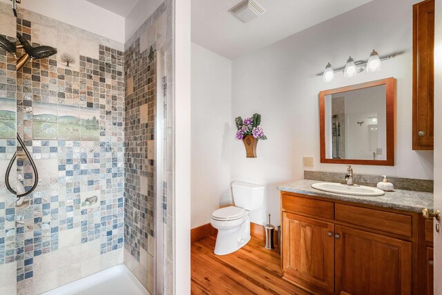 bathroom featuring hardwood / wood-style flooring, tiled shower, vanity, and toilet