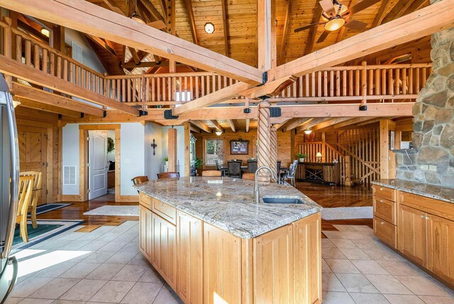 kitchen featuring sink, light stone counters, a large island with sink, beamed ceiling, and ceiling fan