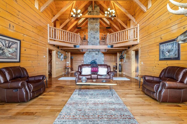 living room featuring a chandelier, high vaulted ceiling, wooden walls, beam ceiling, and light hardwood / wood-style floors