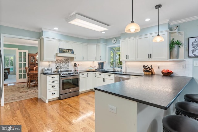 kitchen with white cabinets, dark countertops, a peninsula, stainless steel appliances, and a sink