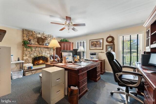 office space featuring ornamental molding, dark colored carpet, a stone fireplace, and a ceiling fan