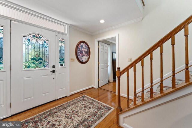 entrance foyer with stairs, visible vents, wood finished floors, and ornamental molding