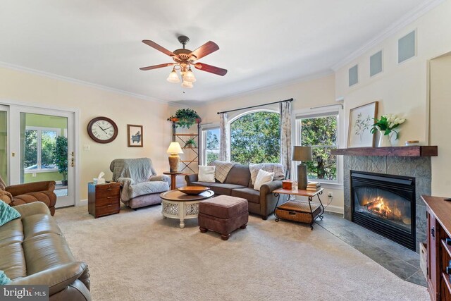 living room featuring a tile fireplace, a ceiling fan, baseboards, ornamental molding, and carpet